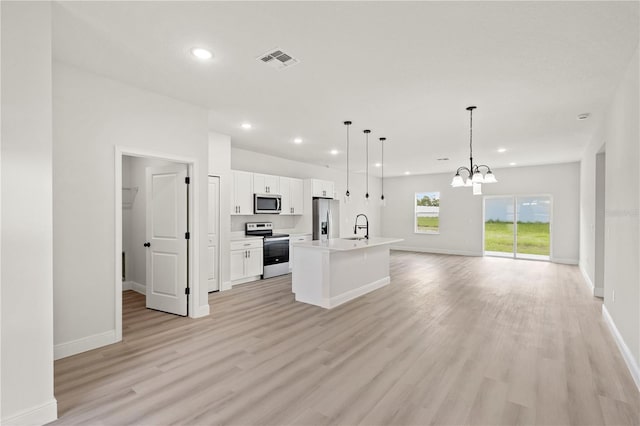 kitchen with appliances with stainless steel finishes, hanging light fixtures, white cabinetry, light hardwood / wood-style flooring, and a kitchen island with sink