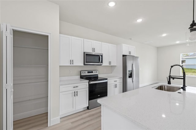 kitchen with sink, white cabinetry, hanging light fixtures, light hardwood / wood-style flooring, and appliances with stainless steel finishes