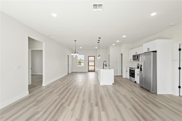 kitchen with appliances with stainless steel finishes, white cabinetry, pendant lighting, light wood-type flooring, and a kitchen island with sink