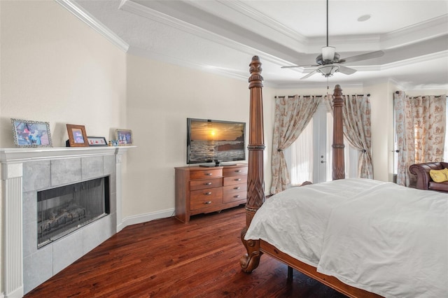 bedroom featuring ornamental molding, dark wood-type flooring, a tile fireplace, and a raised ceiling