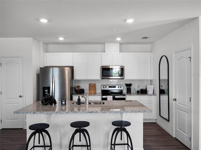 kitchen featuring stainless steel appliances, white cabinets, a sink, and an island with sink