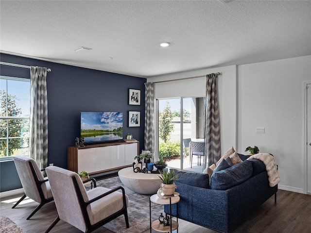 living area with visible vents, a textured ceiling, baseboards, and wood finished floors