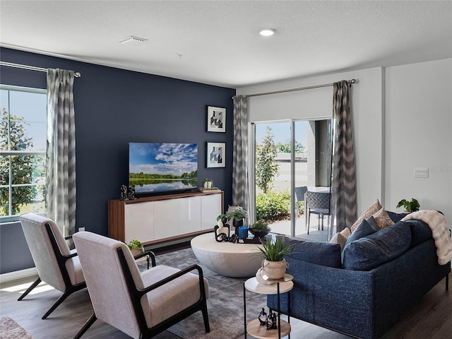 living room featuring baseboards, a textured ceiling, visible vents, and wood finished floors