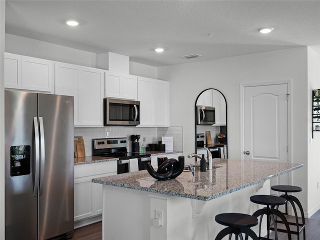 kitchen with stainless steel appliances, white cabinetry, and a center island with sink