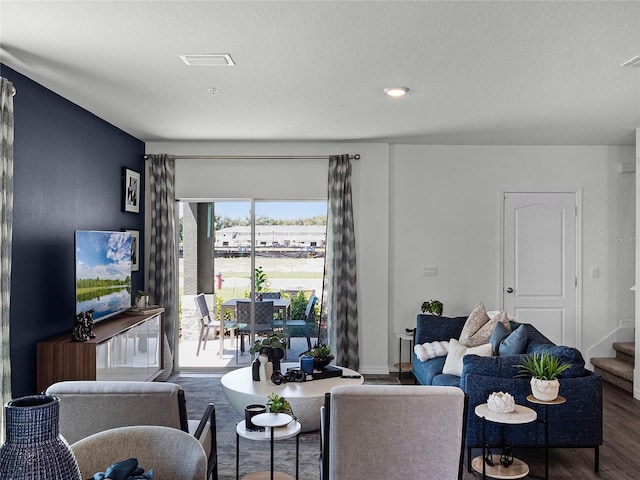 living area with visible vents, a textured ceiling, wood finished floors, baseboards, and stairs