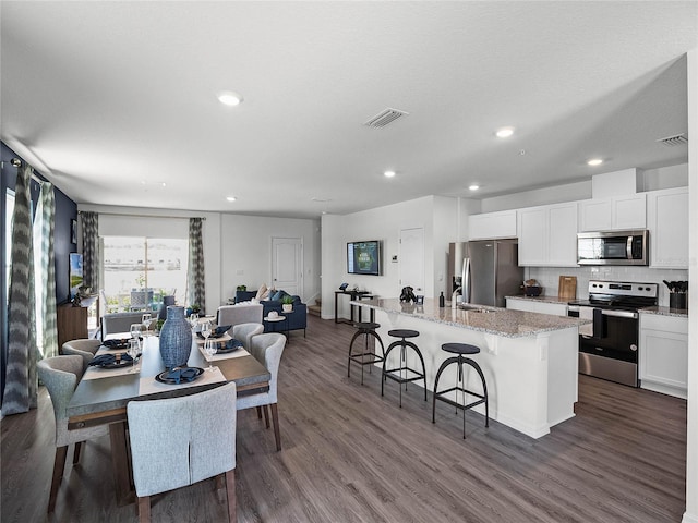 kitchen with open floor plan, a kitchen island with sink, stainless steel appliances, a kitchen bar, and white cabinetry