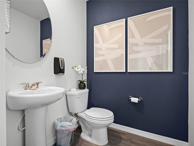 half bathroom with toilet, a sink, baseboards, and wood finished floors