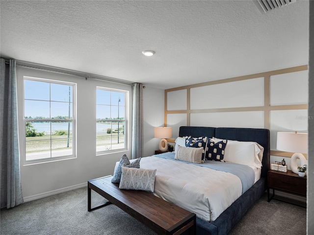 bedroom featuring a textured ceiling, carpet floors, a water view, and visible vents