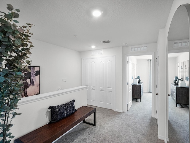 hall with carpet, visible vents, and a textured ceiling