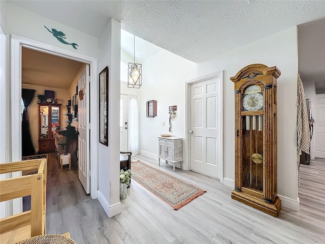 hallway with baseboards, stairway, light wood finished floors, and a textured ceiling