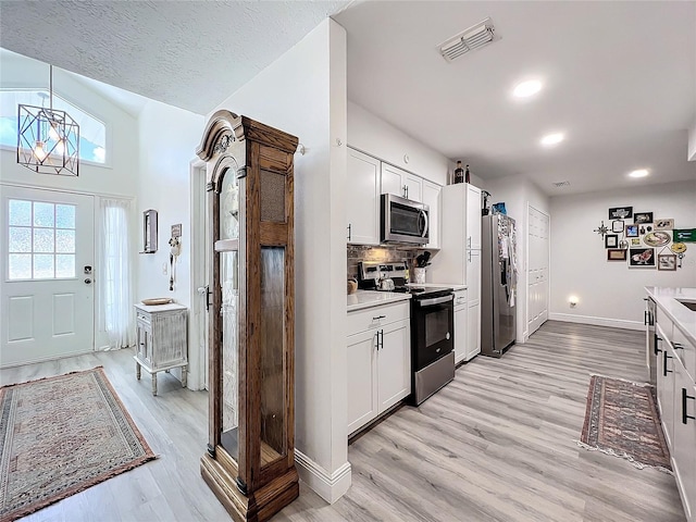 kitchen featuring appliances with stainless steel finishes, light countertops, visible vents, white cabinets, and backsplash