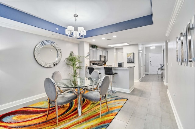 tiled dining room with crown molding, a raised ceiling, and a chandelier