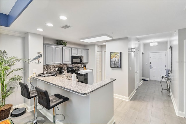 kitchen with light stone countertops, gray cabinetry, decorative backsplash, a kitchen bar, and kitchen peninsula