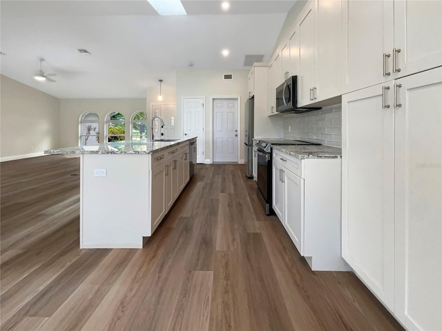 kitchen with white cabinetry, a kitchen island with sink, stainless steel appliances, light stone countertops, and hardwood / wood-style floors