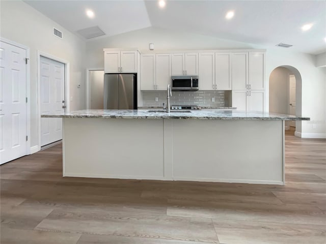 kitchen with white cabinetry, tasteful backsplash, stainless steel appliances, light wood-type flooring, and lofted ceiling