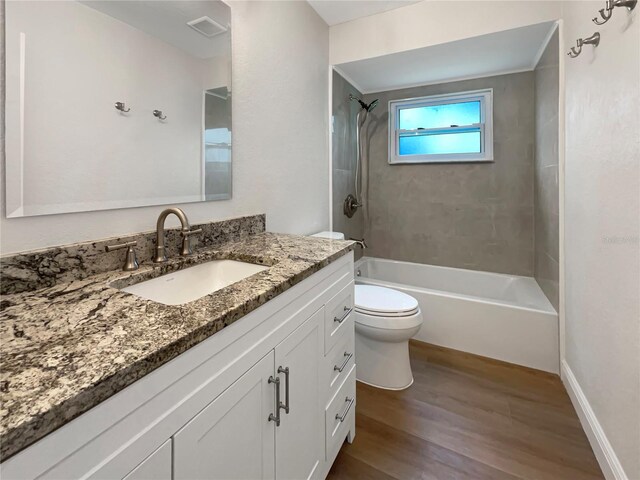 full bathroom featuring wood-type flooring, tiled shower / bath combo, vanity, and toilet