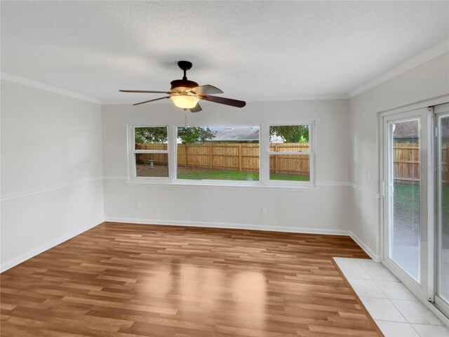 empty room with a healthy amount of sunlight, ceiling fan, light wood-type flooring, and crown molding