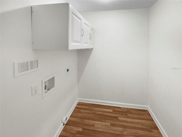 laundry area featuring a textured ceiling, hookup for a washing machine, hardwood / wood-style floors, cabinets, and electric dryer hookup