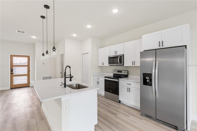 kitchen featuring appliances with stainless steel finishes, hanging light fixtures, an island with sink, light wood-type flooring, and sink