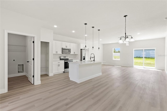 kitchen featuring an island with sink, white cabinets, light hardwood / wood-style flooring, stainless steel appliances, and decorative light fixtures