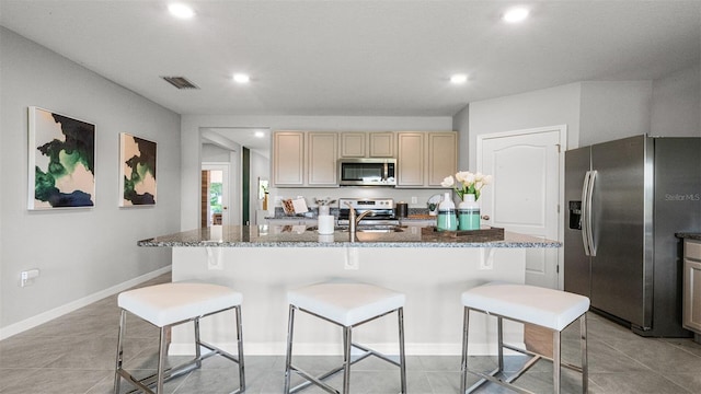 kitchen with appliances with stainless steel finishes, dark stone countertops, a kitchen bar, and an island with sink