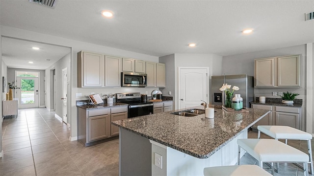 kitchen featuring a kitchen bar, appliances with stainless steel finishes, dark stone counters, sink, and a kitchen island with sink