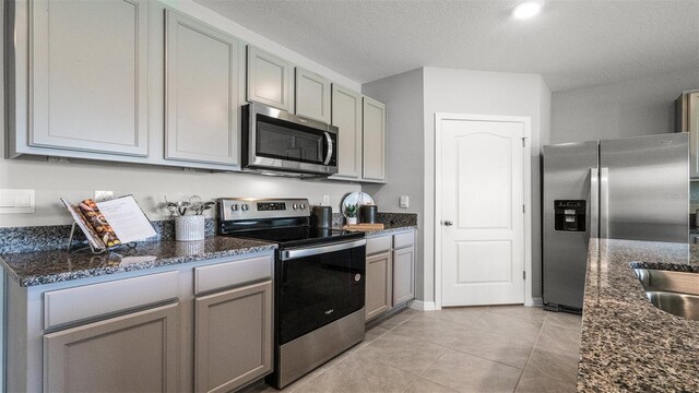 kitchen featuring light tile patterned flooring, appliances with stainless steel finishes, dark stone counters, and gray cabinets