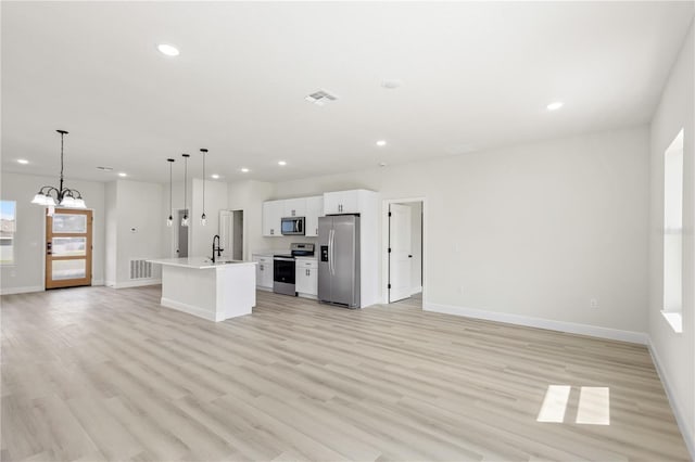 kitchen featuring appliances with stainless steel finishes, white cabinetry, light hardwood / wood-style floors, decorative light fixtures, and a kitchen island with sink