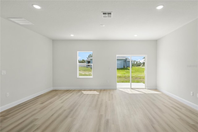 empty room featuring a wealth of natural light, a textured ceiling, and light hardwood / wood-style floors