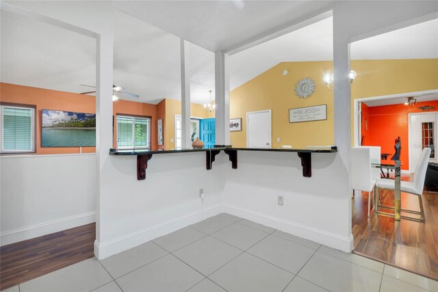 kitchen featuring a breakfast bar area, tile patterned flooring, ceiling fan with notable chandelier, and lofted ceiling