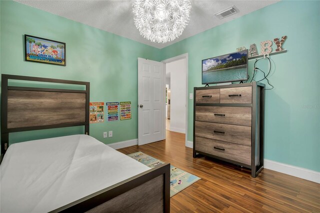 bedroom featuring an inviting chandelier, dark hardwood / wood-style floors, and a textured ceiling