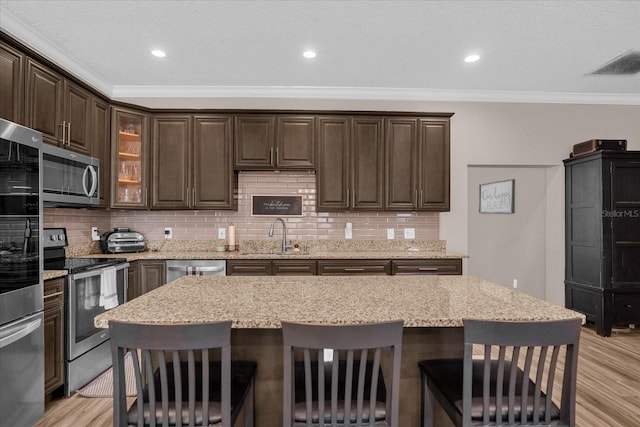 kitchen with dark brown cabinetry, sink, stainless steel appliances, light hardwood / wood-style flooring, and a kitchen bar