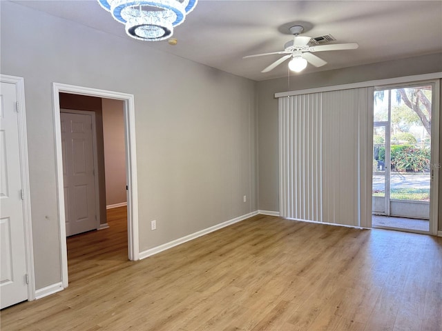 empty room featuring ceiling fan with notable chandelier and light hardwood / wood-style flooring