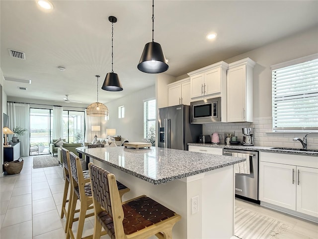 kitchen featuring appliances with stainless steel finishes, light stone counters, hanging light fixtures, white cabinetry, and a sink