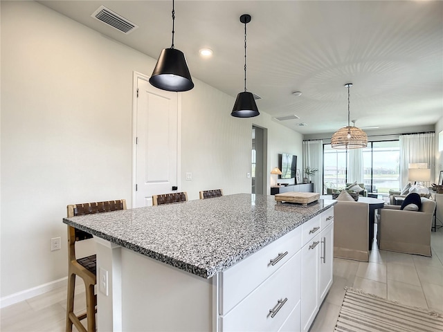 kitchen with a breakfast bar, visible vents, open floor plan, white cabinets, and light stone countertops