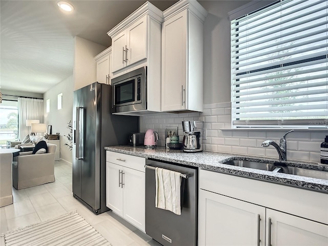 kitchen featuring white cabinets, appliances with stainless steel finishes, open floor plan, a sink, and backsplash