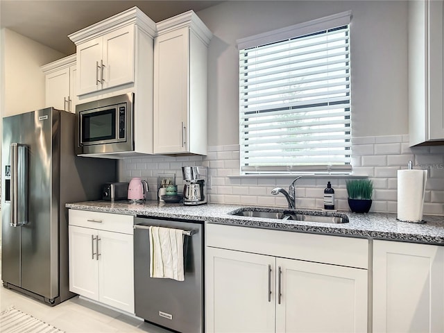 kitchen featuring decorative backsplash, white cabinets, light stone counters, appliances with stainless steel finishes, and a sink