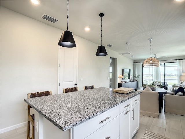 kitchen featuring visible vents, white cabinetry, open floor plan, a center island, and a kitchen bar