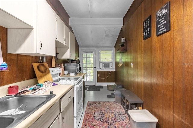 kitchen with white range with electric stovetop, light countertops, white cabinetry, a sink, and wood walls