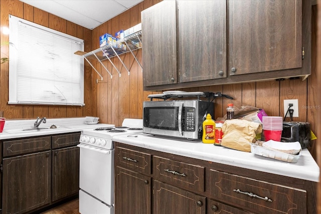 kitchen with wooden walls, stainless steel microwave, dark brown cabinets, light countertops, and white range with electric cooktop