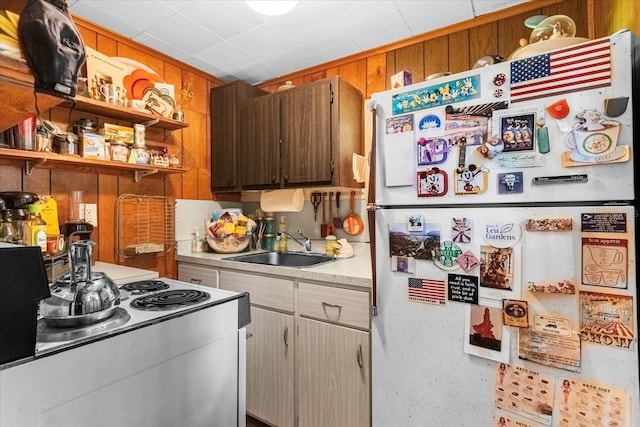 kitchen featuring brown cabinets, light countertops, a sink, wooden walls, and white appliances