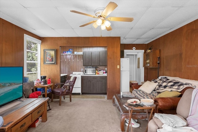 living area with wood walls, ceiling fan, washer / dryer, and light colored carpet