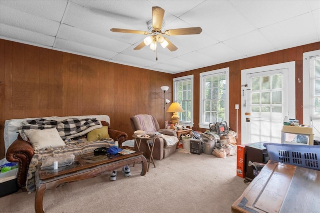 living area with wood walls, ceiling fan, and carpet flooring