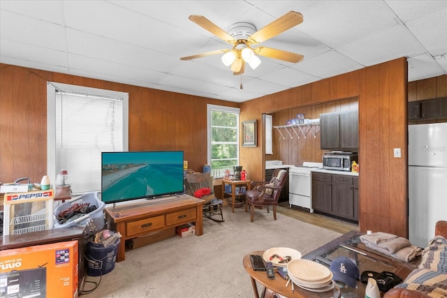 interior space with light carpet, ceiling fan, wooden walls, and a drop ceiling