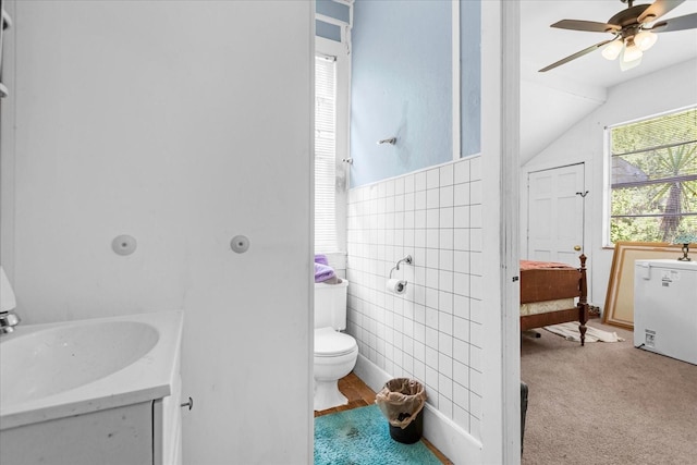 bathroom featuring ceiling fan, lofted ceiling, toilet, vanity, and tile walls