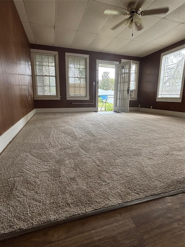 carpeted spare room with wooden walls, baseboards, and a ceiling fan