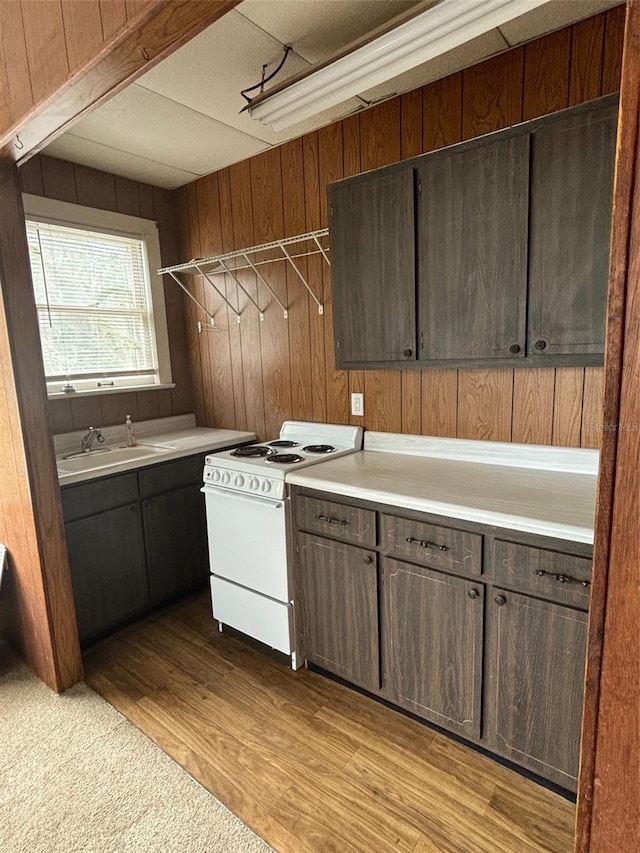 kitchen featuring dark brown cabinets, wooden walls, light countertops, and white range with electric cooktop