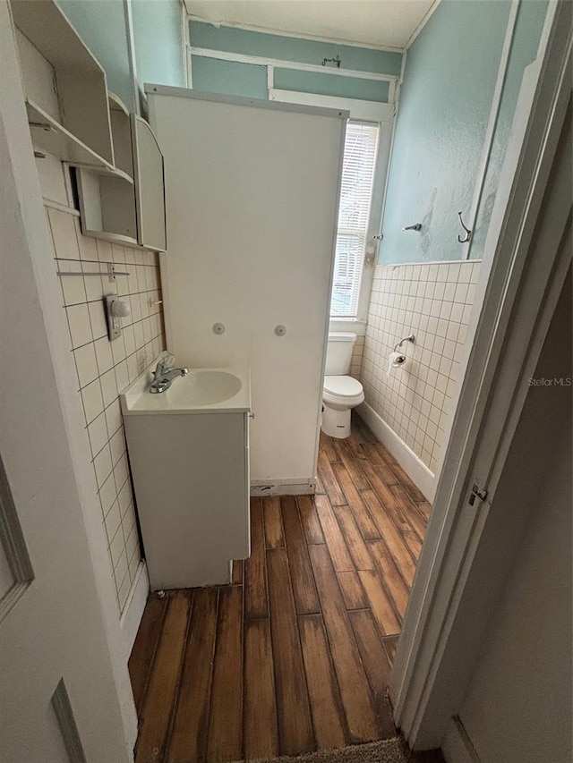 half bath featuring wainscoting, toilet, wood finished floors, vanity, and tile walls