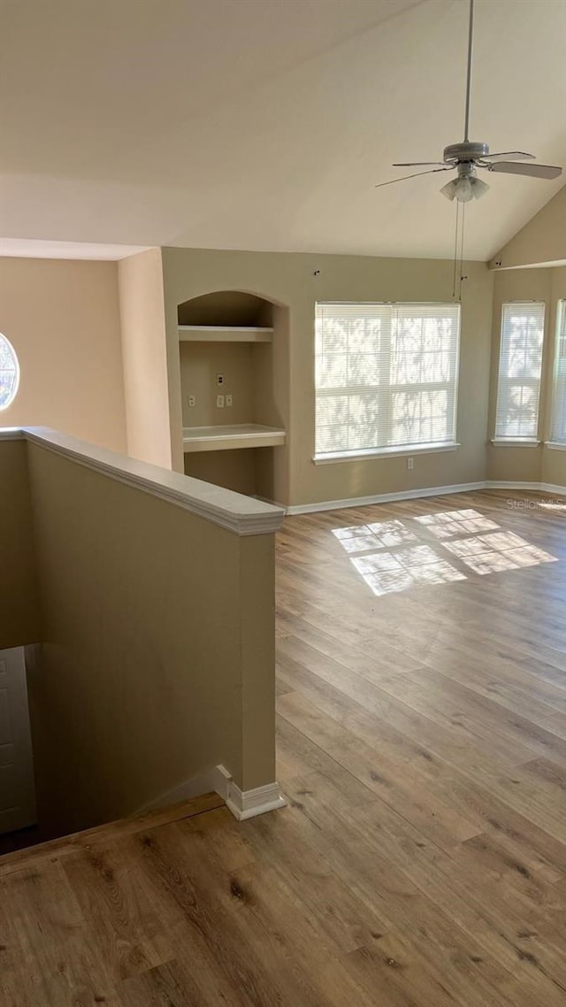 empty room featuring built in features, light hardwood / wood-style flooring, vaulted ceiling, and ceiling fan