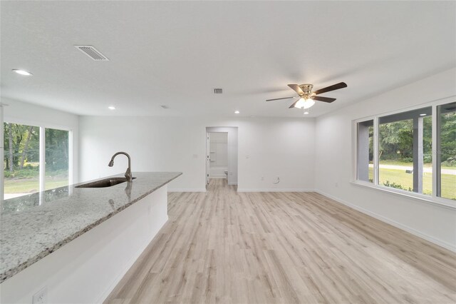 unfurnished living room with sink, light hardwood / wood-style flooring, ceiling fan, and plenty of natural light